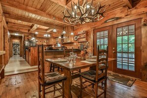 Un'accogliente sala in legno rustico con un tavolo da pranzo apparecchiato per quattro persone, un lampadario e un'ampia finestra vista su un paesaggio verde.