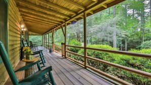 Eine überdachte Veranda mit Holzbalkonen, grünen Stühlen und einem Tisch mit Blumen.
