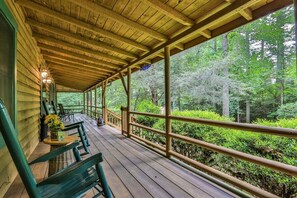Un portico coperto con ringhiere in legno, sedie verdi e un tavolo con fiori.