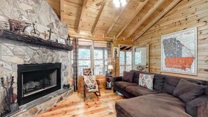 A cozy cabin interior with a stone fireplace, wooden floors, a sofa, and a map on the wall.