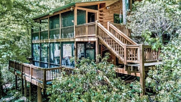 A wooden cabin with a glass-enclosed upper deck and a staircase leading to the entrance.