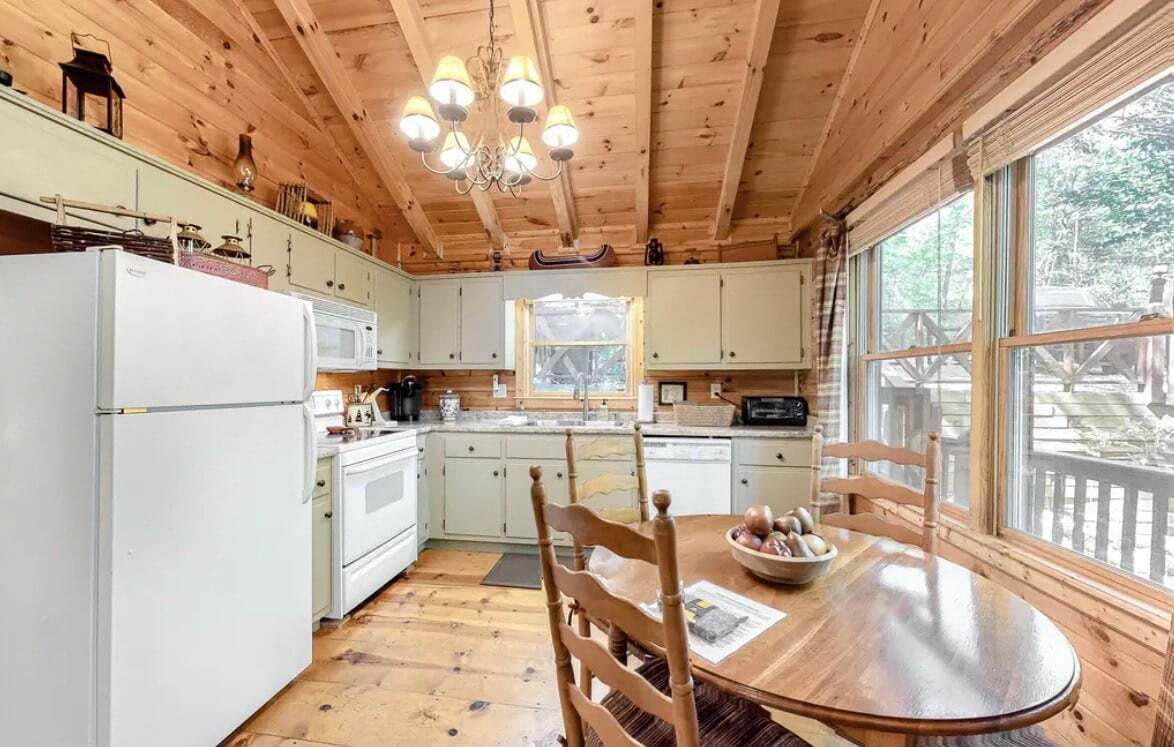 Interior de una cabaña de madera con cocina, comedor y ventanas amplias.