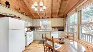 A wooden cabin interior with a kitchen, dining area, and large windows.