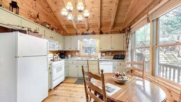 Interior de una cabaña de madera con cocina, comedor y ventanas amplias.