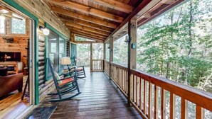 A log cabin with a wooden porch, rocking chairs, and a fireplace.