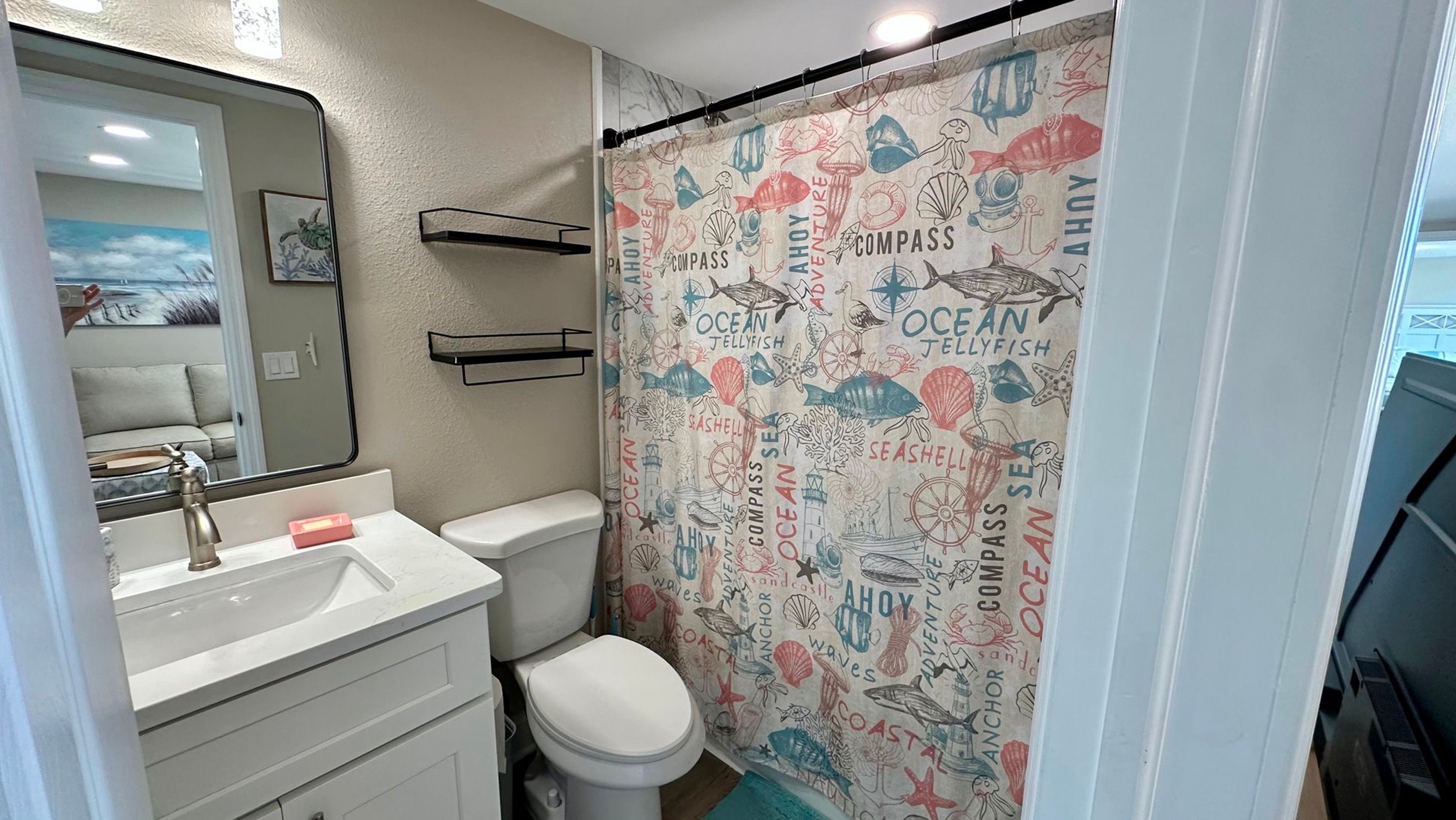 A bathroom with a white sink, a toilet, and a shower curtain with nautical illustrations.