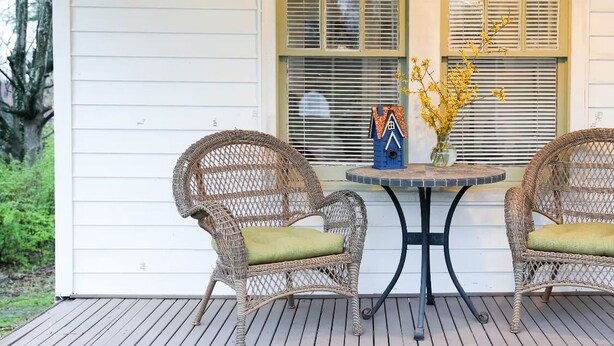 A porch with wicker chairs and a table, a birdhouse, and a vase with yellow flowers. - Jude's cozy & convenient downtown studio Apt. (High Point)