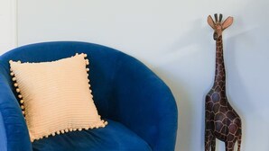 A room with a blue armchair, a framed floral artwork, and a giraffe sculpture. - Jude's cozy & convenient downtown studio Apt. (High Point)