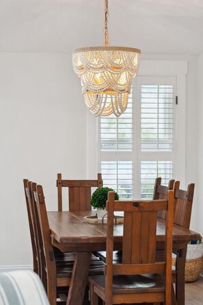 Un coin repas avec une table et des chaises en bois, un lustre décoratif et une fenêtre avec des stores.