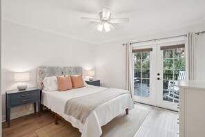 Une chambre à coucher comprenant un lit, des tables de chevet, un ventilateur de plafond et une vue sur une terrasse extérieure, accessible par une porte-fenêtre coulissante.
