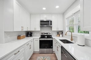 Cocina moderna con gabinetes blancos, estufa de acero inoxidable, microondas y pileta con grifo dorado.