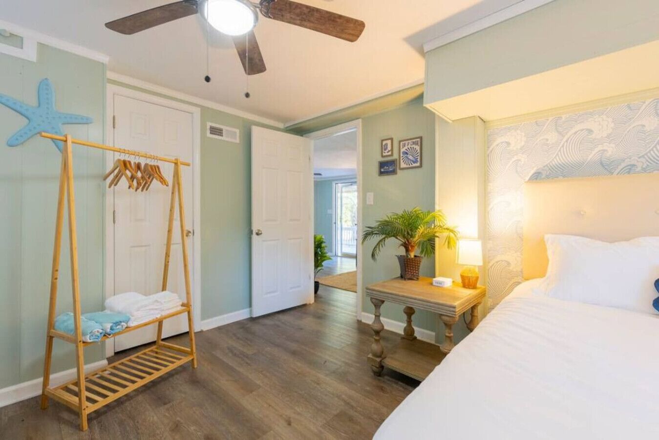 A bedroom with a bed, a wooden swing chair, a nightstand with a lamp, and a starfish decoration on the wall.