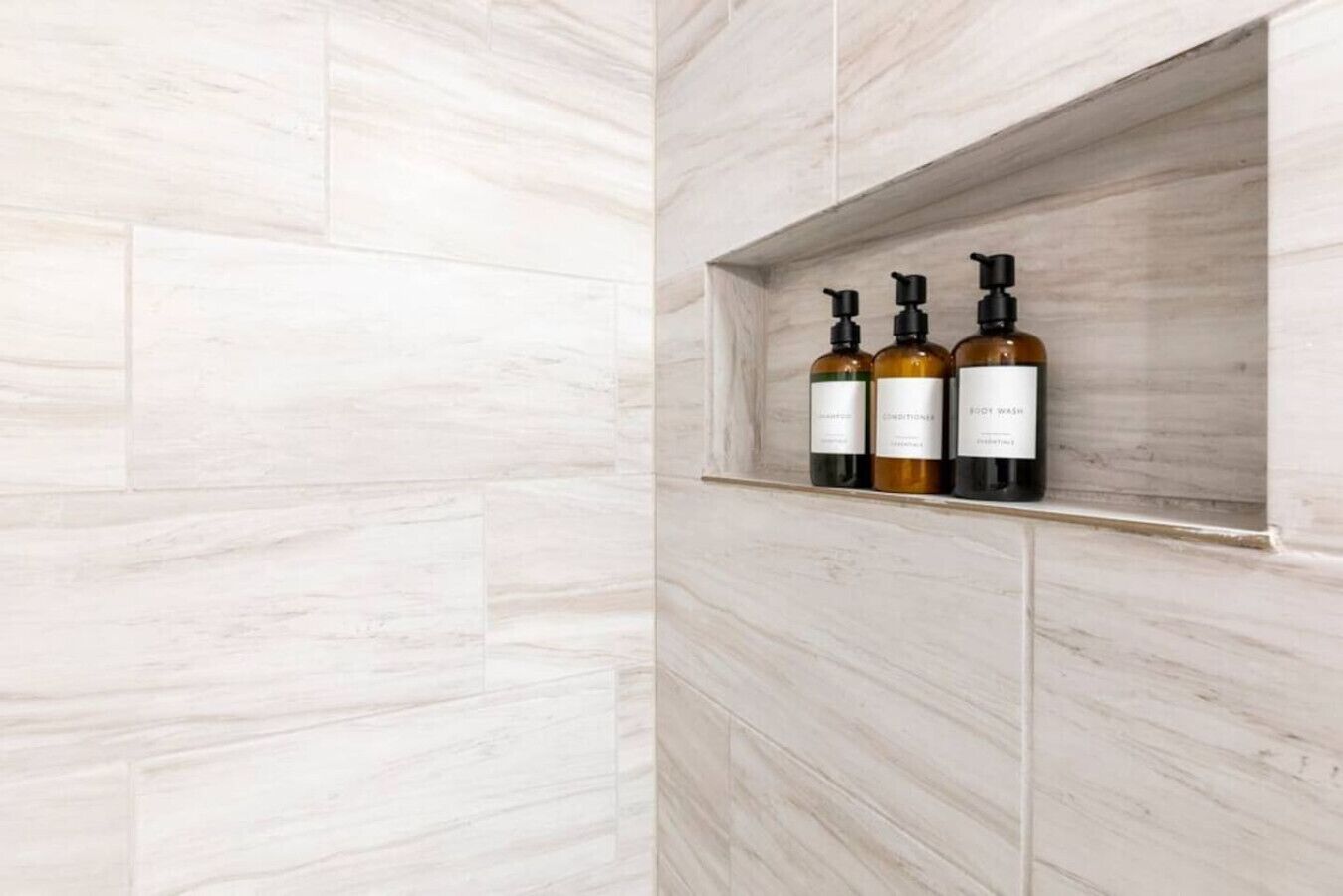 Een badkamer met een lichtkleurige marmeren wand en een plank met drie flessen toiletartikelen.