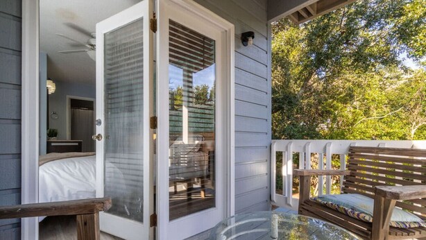 A glass-enclosed patio with a sliding door leading to a bedroom, a glass table, and a wooden bench. - Point Oasis|Golf Cart·The Point Beach·Sleeps 7·EI (Emerald Isle)