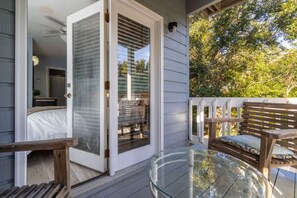 Ein verglaster Patio mit einer Schiebetür zum Schlafzimmer, einem Glastisch und einer Holzbank.