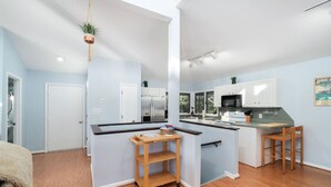 A compact kitchen with modern appliances, a small dining area, and a visible door leading to another room. - Point Oasis|Golf Cart·The Point Beach·Sleeps 7·EI (Emerald Isle)