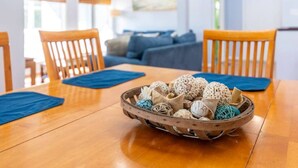 A dining table with a wooden finish, a basket of decorative items, and blue placemats. - Point Oasis|Golf Cart·The Point Beach·Sleeps 7·EI (Emerald Isle)