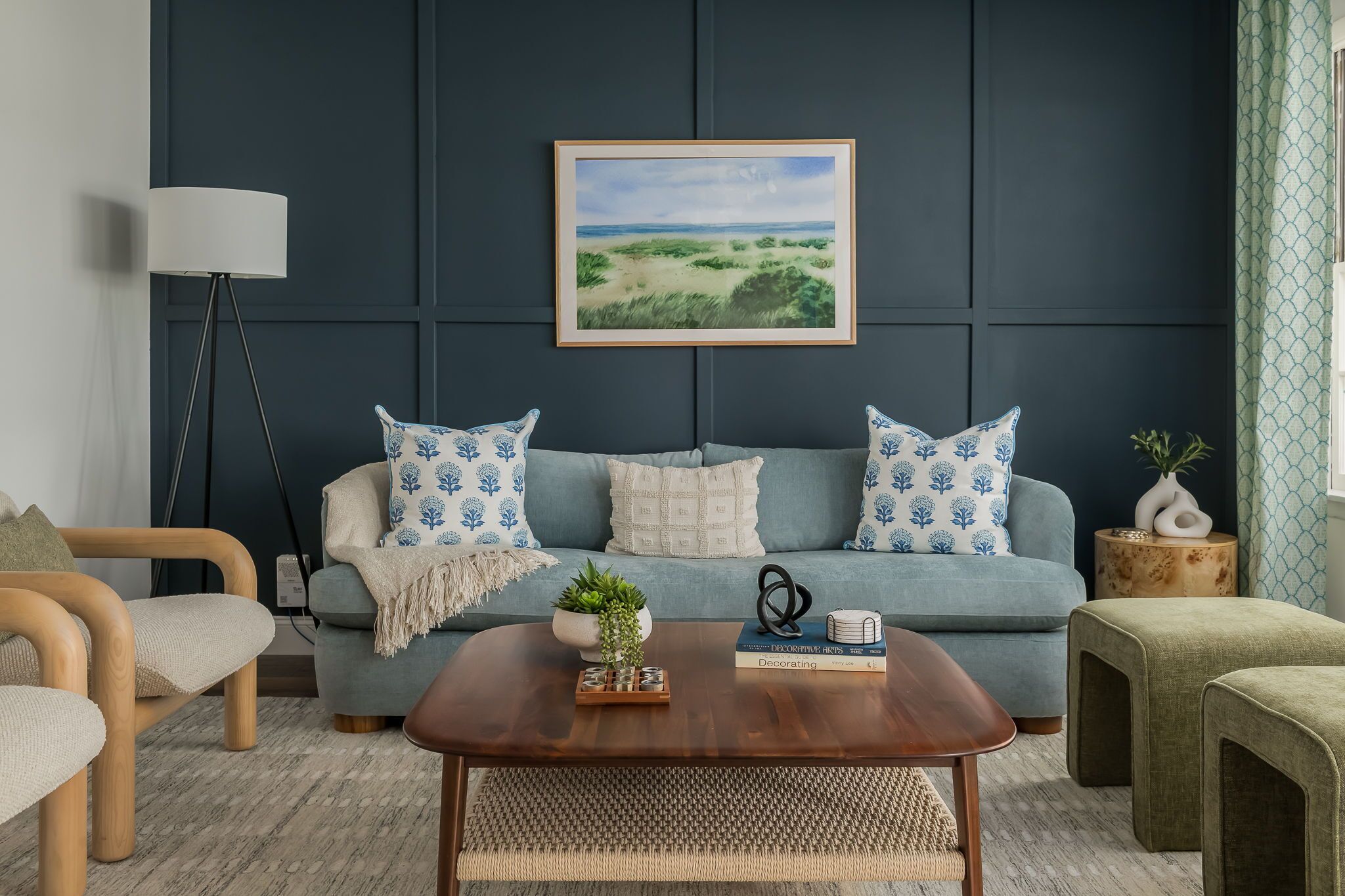 Un salon moderne avec un mur bleu foncé, un canapé bleu clair agrémenté de coussins à motifs, une table basse en bois et un tableau représentant un paysage, encadré.