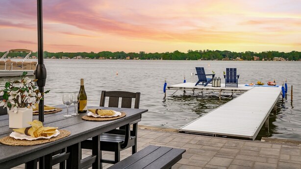 Un espace de restauration situé au bord de l’eau, avec une table dressée pour deux personnes, une bouteille de vin et un arrangement floral.