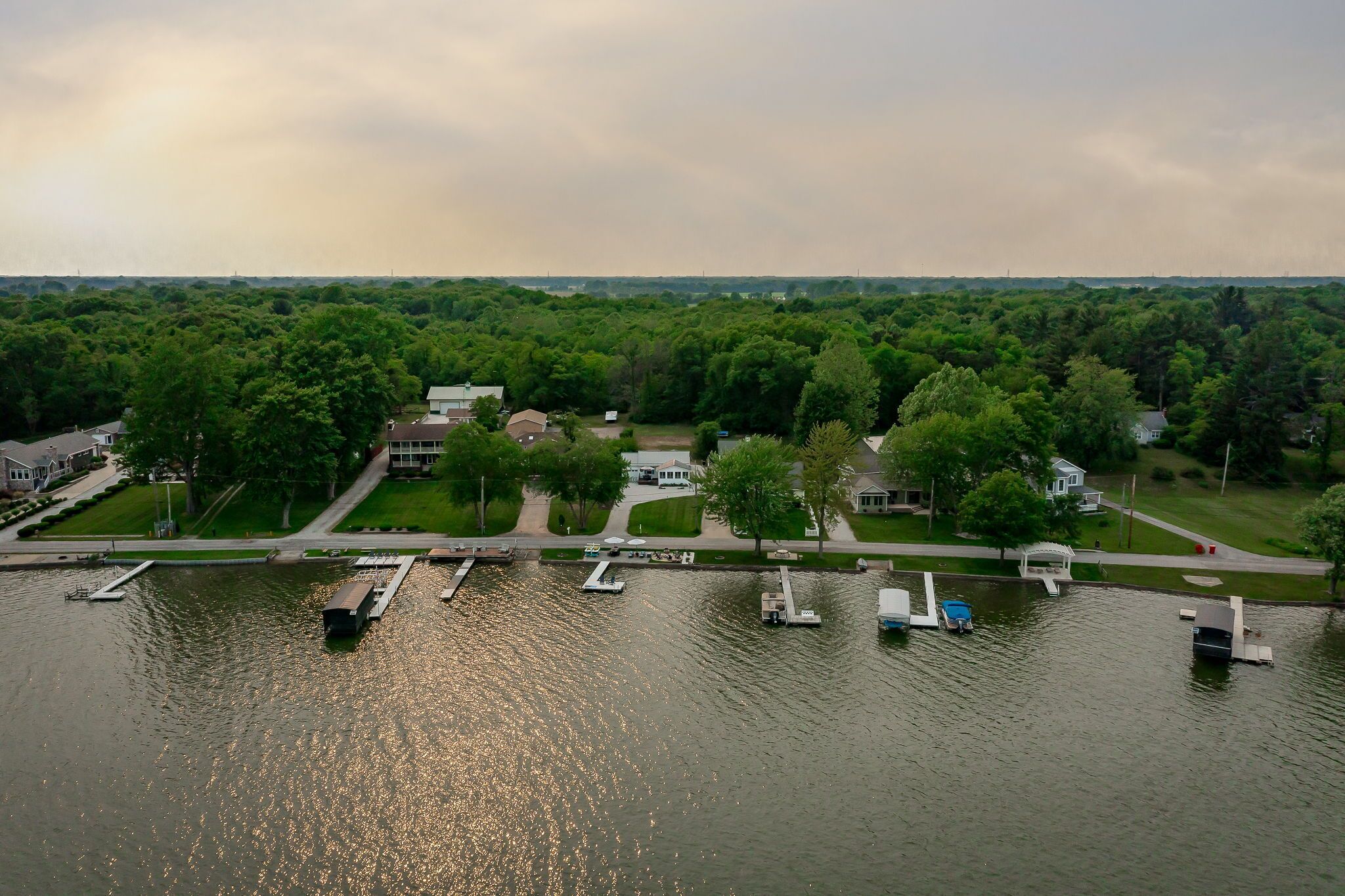 An aerial view of a lakeside property with docked boats, a marina, and surrounding greenery.