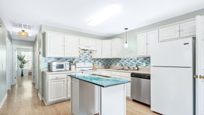 Une cuisine moderne avec des meubles blancs, un îlot central, un four à micro-ondes, une cuisinière et un réfrigérateur.
