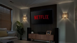 Un salon moderne avec un grand téléviseur à écran plat fixé au mur, deux haut-parleurs également fixés au mur, une console en bois, un canapé et une plante en pot.