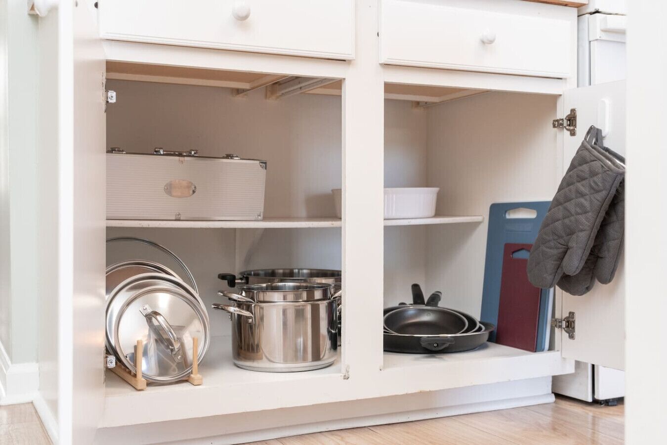 A kitchen cabinet with pots, pans, and a kettle.