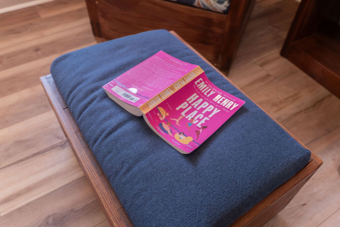 Un livre intitulé « Happy Place » de Henry, posé sur un banc en bois avec un coussin sombre.