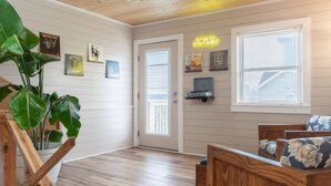 A room with a wooden floor, a wooden ceiling, a door, a bench, and a wall with framed pictures. - Cabin by the Sea|1-Min Beach·Projector Room·Log Cabin EI (Emerald Isle)