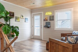 Een kamer met een houten vloer, een houten plafond, een deur, een bankje en een muur met ingelijste foto's.