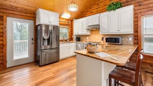A modern kitchen with wooden walls, a stainless steel refrigerator, white cabinets, and a granite countertop. - Cabin by the Sea|1-Min Beach·Projector Room·Log Cabin EI (Emerald Isle)