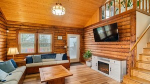 A log cabin interior with a sofa, coffee table, fireplace, TV, and wooden staircase. - Cabin by the Sea|1-Min Beach·Projector Room·Log Cabin EI (Emerald Isle)