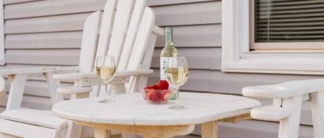 A white wooden table with two glasses of white wine and a bowl of strawberries.