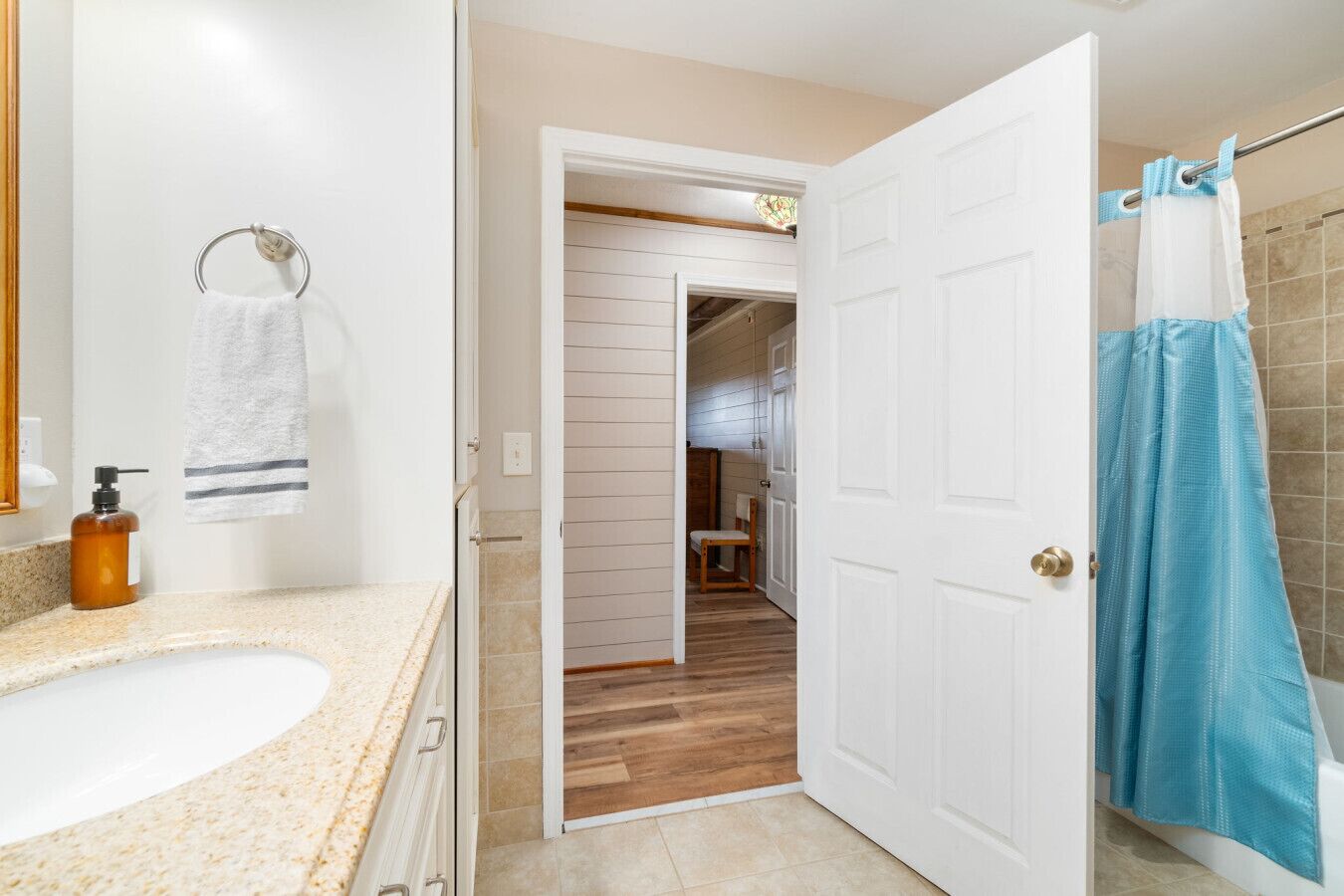 Une salle de bain avec un lavabo blanc, un porte-serviettes, un rideau de douche bleu et un plancher en bois.