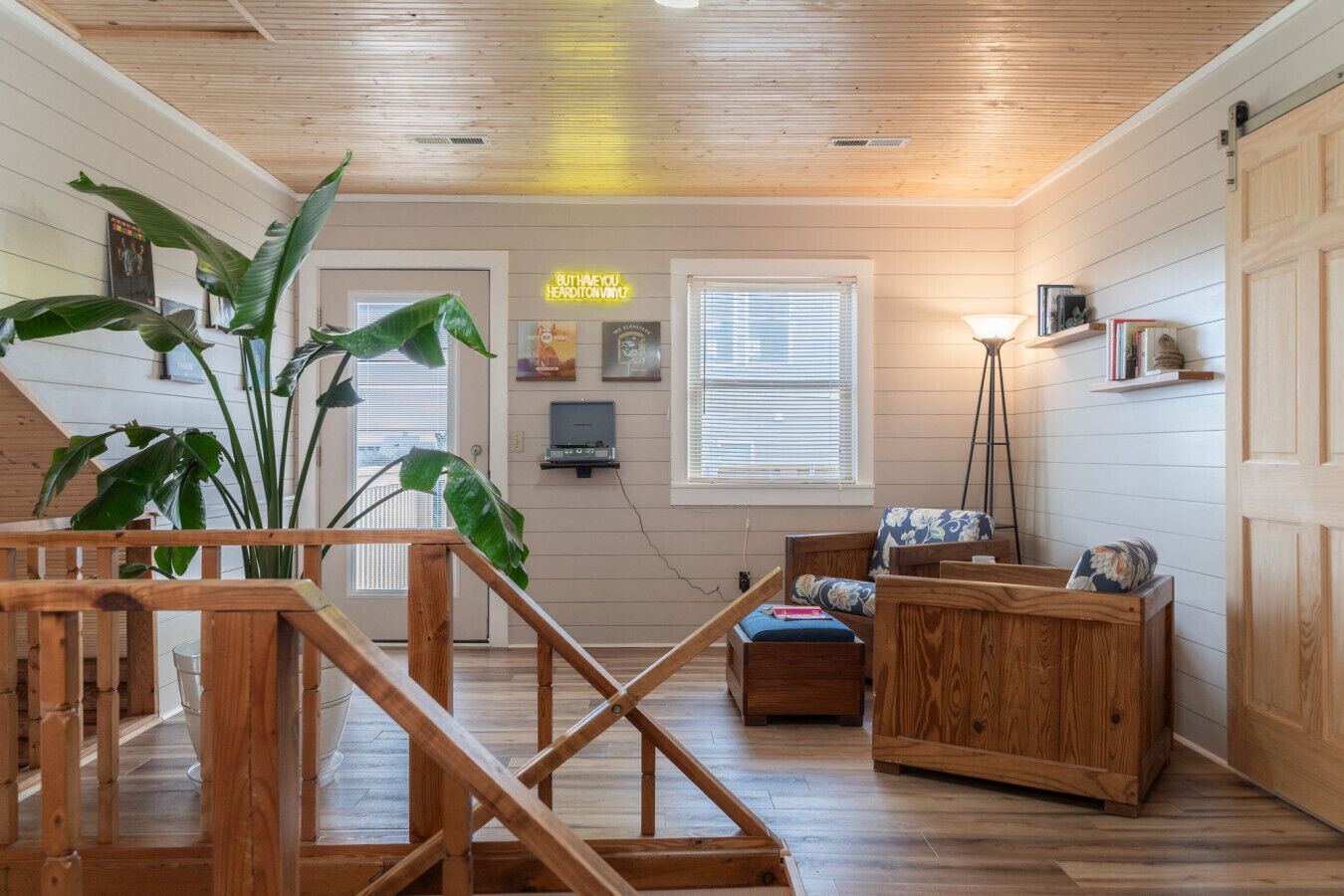 Une pièce chaleureuse avec un plancher en bois, un escalier, une grande plante, un canapé et un bureau.