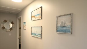 Ein Flur mit drei gerahmten Kunstwerken, die Meerlandschaften zeigen, und einem runden Spiegel an der Wand.