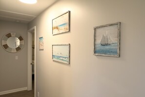A hallway with three framed artworks depicting seascapes and a circular mirror on the wall.