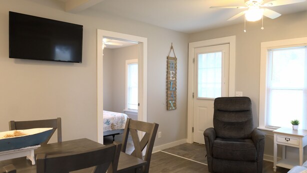 A modern living room with a flat-screen TV, a dark armchair, a dining table with chairs, and a small side table. - Spacious 3BR Retreat | Perfect for Families! (Indian River)