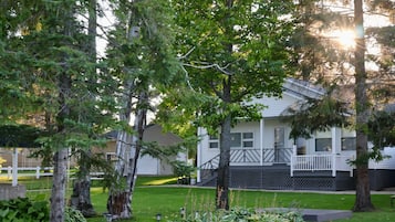 Une maison d’habitation dotée d’un porche à l’avant, entourée d’arbres et d’une pelouse bien entretenue.