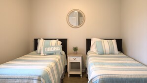 A bedroom with two beds, each with striped bedding and a pillow with the word "BEACH". There is a small bedside table with a plant and a mirror on the wall above the beds. - Spacious 3BR Retreat | Perfect for Families! (Indian River)