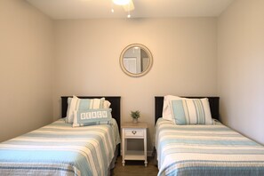 A bedroom with two beds, each with striped bedding and a pillow with the word "BEACH". There is a small bedside table with a plant and a mirror on the wall above the beds. - Spacious 3BR Retreat | Perfect for Families! (Indian River)