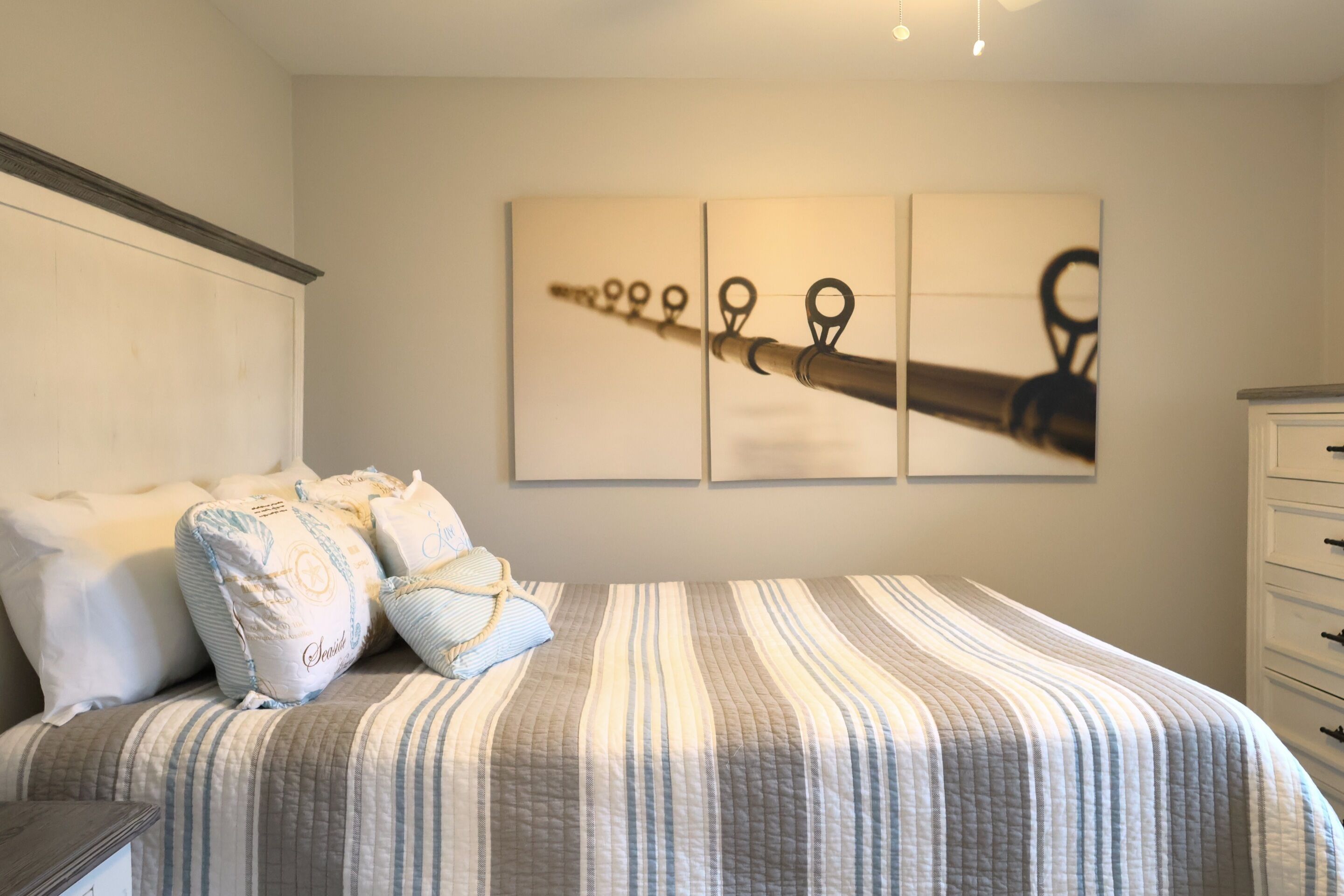Une chambre à coucher avec un lit, des oreillers, une commode et un mur orné de trois tableaux encadrés.