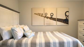 Une chambre à coucher avec un lit, des oreillers, une commode et un mur orné de trois tableaux encadrés.