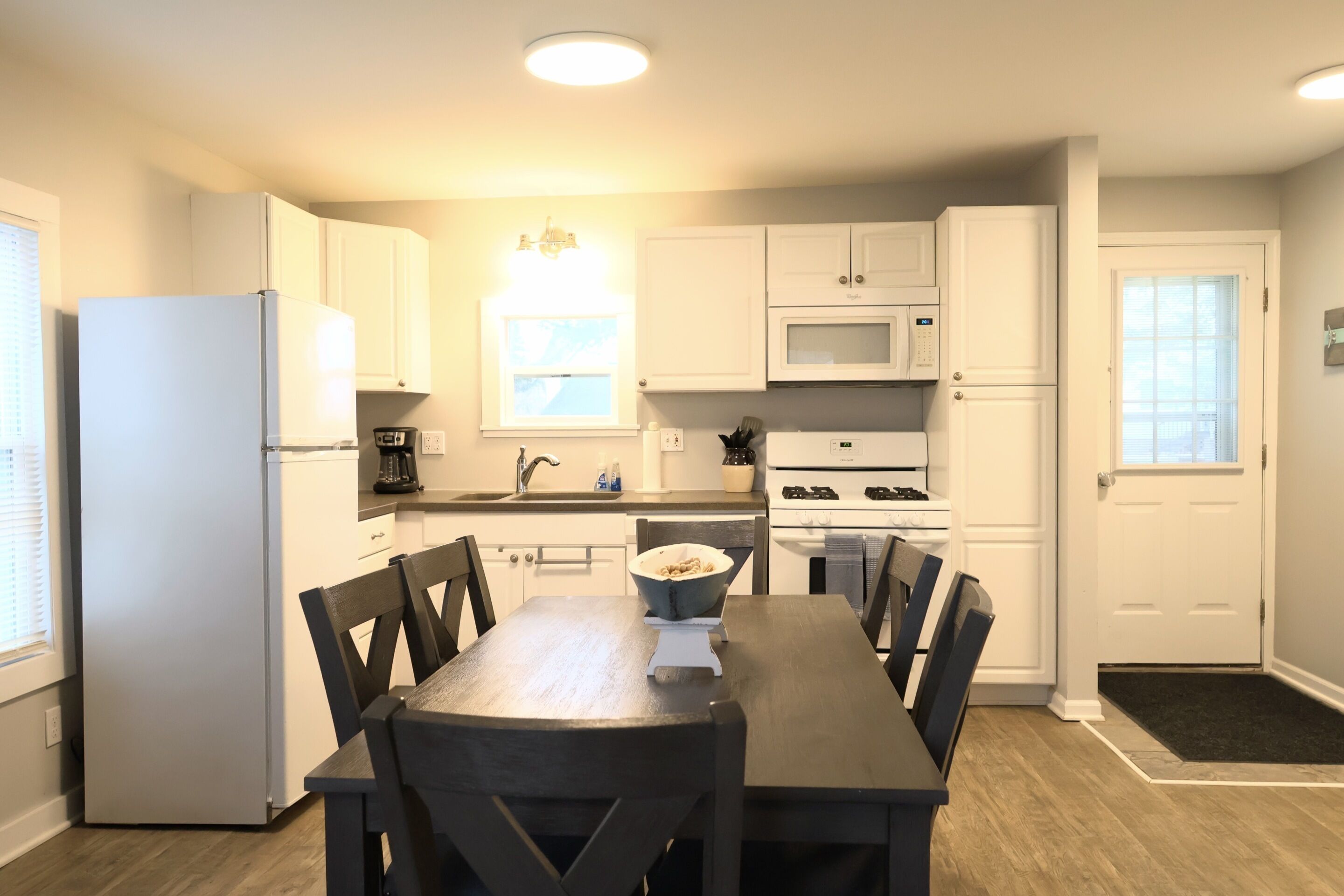 A compact kitchen with white cabinets, a microwave, a stove, and a dining table with chairs.