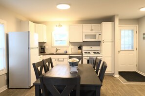 A compact kitchen with white cabinets, a microwave, a stove, and a dining table with chairs. - Spacious 3BR Retreat | Perfect for Families! (Indian River)