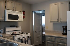 A kitchen with white cabinets, a stove, a microwave, a sink, and a coffee maker.