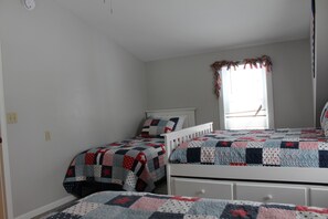 A bedroom with two single beds, a window with a curtain, and a white wall.