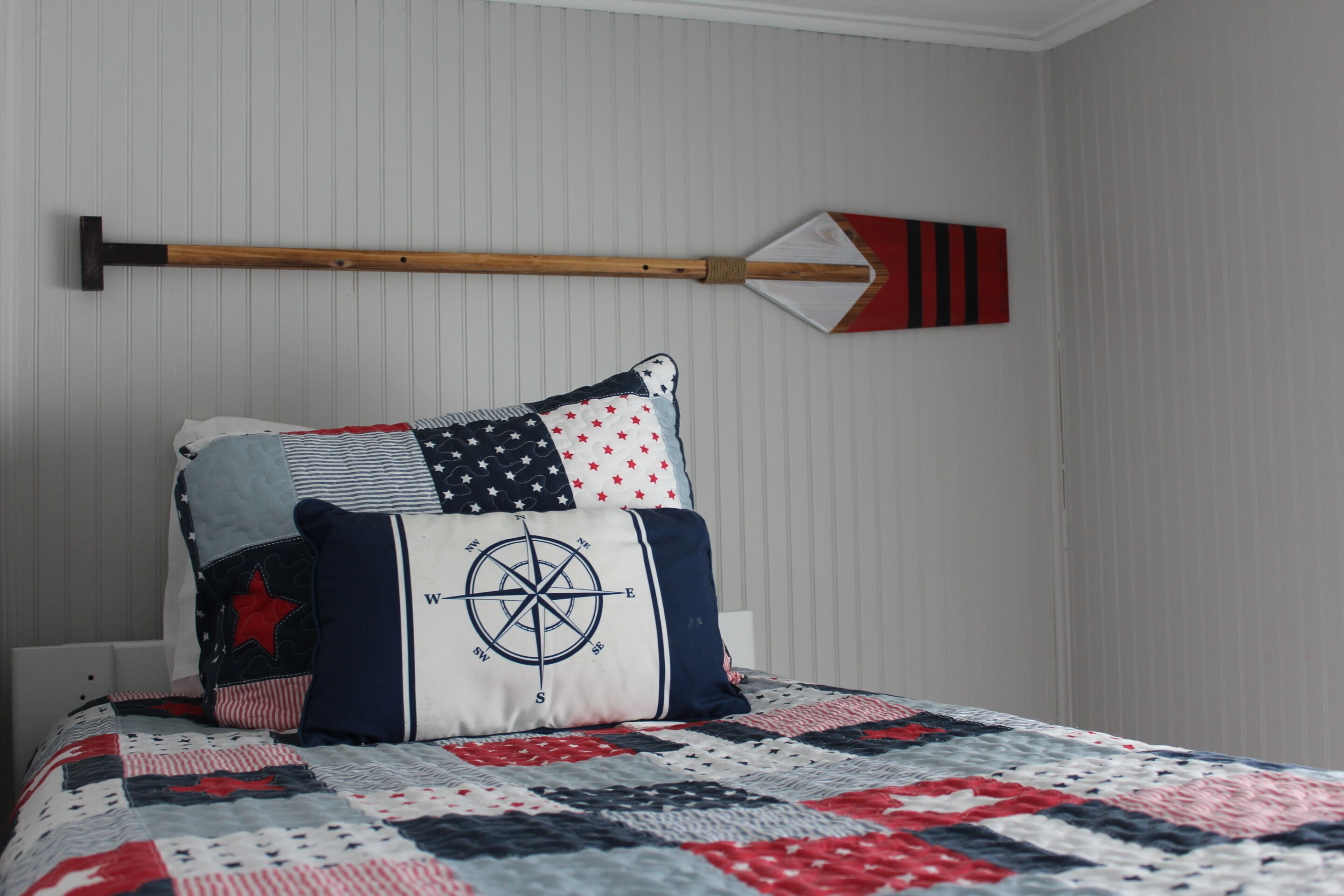 Un lit avec une courtepointe ornée d’un motif patriotique, un oreiller en forme de boussole et une pagaie décorative fixée au mur.