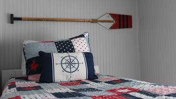 Un lit avec une courtepointe ornée d’un motif patriotique, un oreiller en forme de boussole et une pagaie décorative fixée au mur.