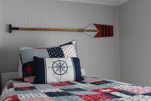 Een bed met een deken met een patriottisch motief, een kussen met een kompas en een op de muur bevestigd roeispaak.
